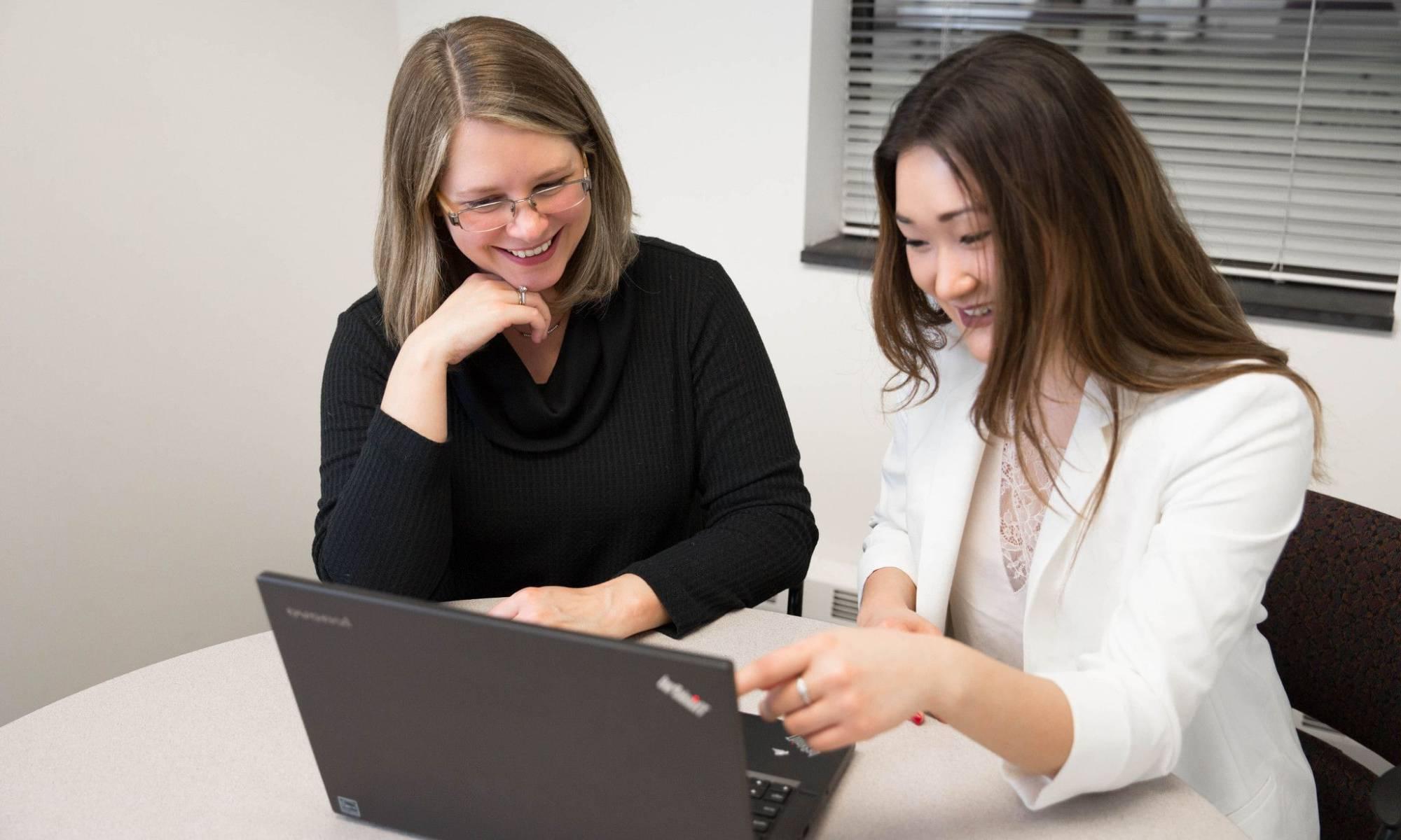 Professor and student sitting at table with laptop computer